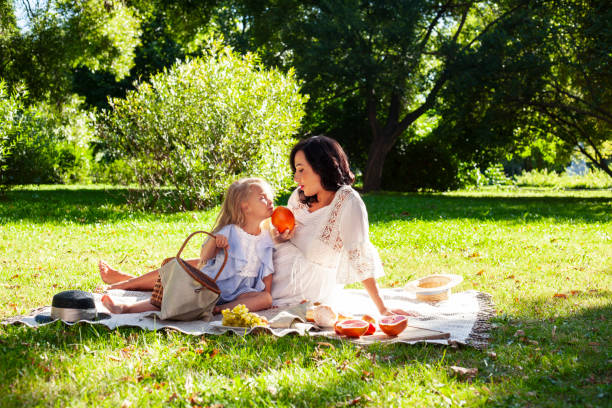 young pretty pregnant brunette woman having fun with her daughter on picnic on green grass in park, lifestyle people concept stock photo
