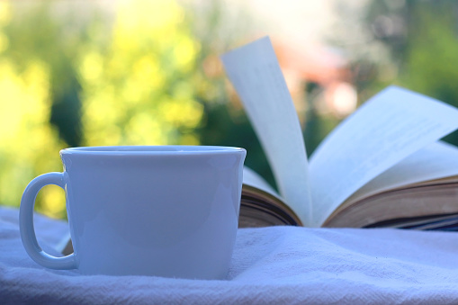 Cup of coffee or tea and open book on a table outdoor. Selective focus.
