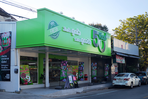 New small fresh food supermarket in Bangkok in area of Nawamin / Senanikhom. Top part of building is green colored with logo. A car is parked in street