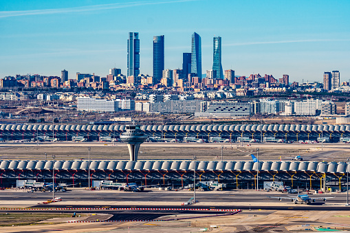 Madrid, Spain - December 31, 2021: Control tower of Adolfo Suarez Madrid-Barajas airport against cityscape with Cuatro Torres Business Area skyscrapers