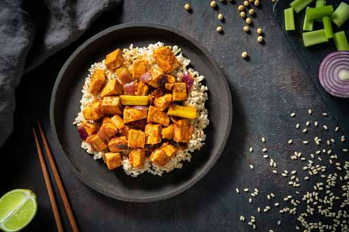 Stir-fried tofu with Brown rice vegan plant based asian recipe with ingredients as sesame oil, tofu, corn starch, black pepper, maple syrup, gochujang, soy sauce, rice vinegar, garlic, chili, onion, sesame seeds, celery