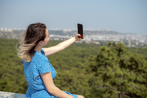 Beautiful young woman taking selfies while hiking up a mountain. Horizontal composition.