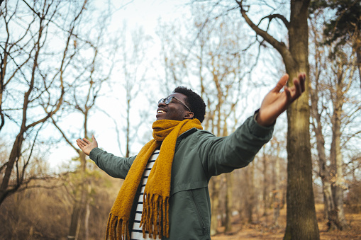 Black man breathing fresh air stretching arms in a park. Shot of a man standing outside with his arms outstretched in delight. Handsome man is standing in the mountains with his arms wide open