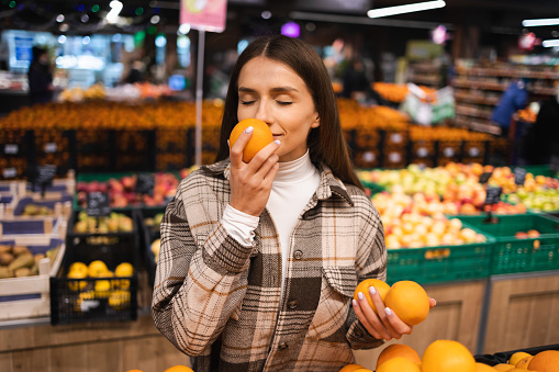 Portrait of a young woman picking oranges in a supermarket. Woman smelling fresh oranges fruit at grocery store
