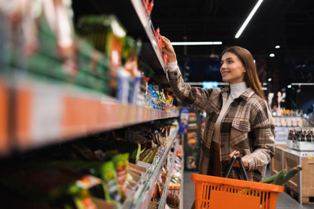 Happy young woman looking at product at grocery shop. Customer buying food at the supermarket Happy young woman looking at product at grocery shop. Customer buying food at the supermarket holding shopping basket stock pictures, royalty-free photos & images