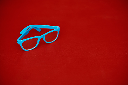 Pair of modern blue eyeglasses on a red background with space for copy