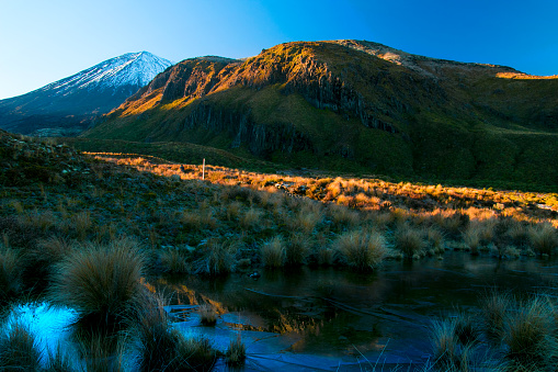Ice cold morning in the wild nature, sunrise blue hour, frozen waters in the front, mountains and volcano in the back, Tongariro crossing, hiking track spot near Mangatepopo car park