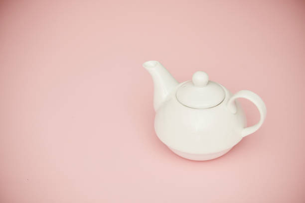 White china teapot on pink background with copy space