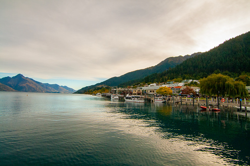 Resort town in mountains of Southern Alps on the lake Wakatipu, Queenstown harbor with dock boats and lakeside promenade, Walter Peak on background, New Zealand South Island