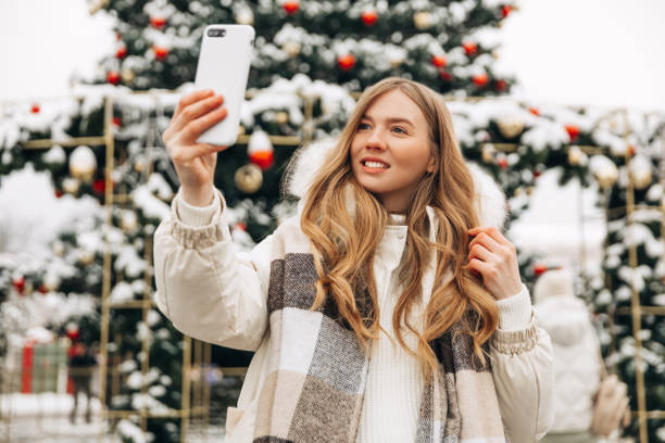 istock Beautiful woman, makes a selfie or emotionally talks on a mobile phone outdoors in front of Christmas decorations 1363647013