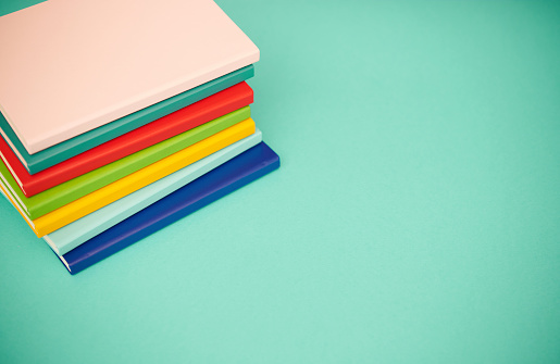 Stack of brightly colored books on a teal background with space for copy