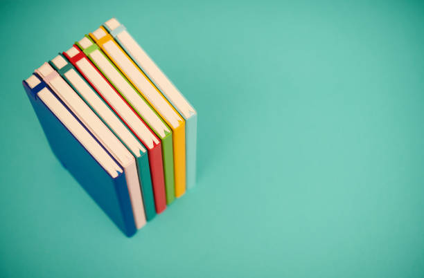 Stack of brightly colored books on a teal background with space for copy