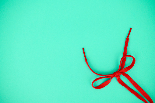 Red shoelaces tied in a bow on a vibrant teal background with space for copy