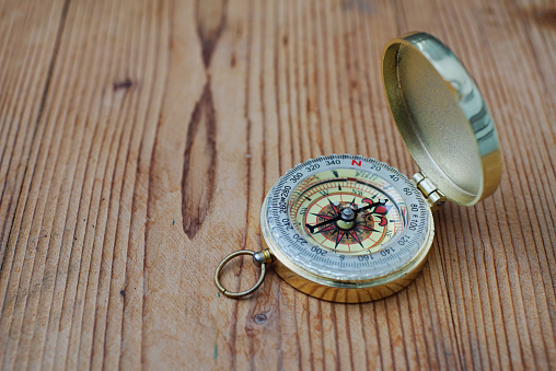 Close up shot of a vintage brass compass on wooden background.