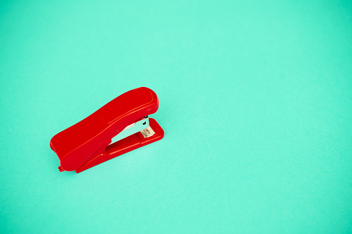 Red stapler on teal background with copy space