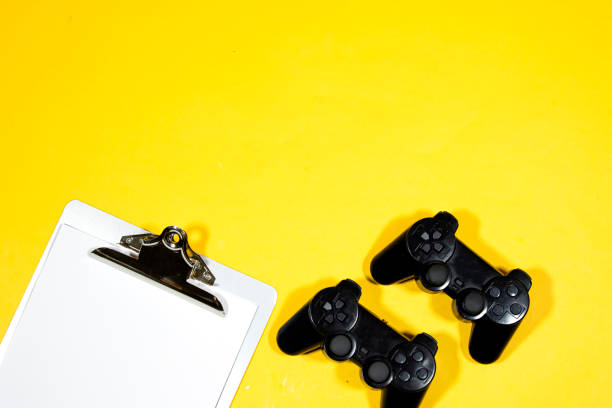 istock black joysticks, game controller with Classic metal clipboard with blank white paper isolated on yellow background 1363652744