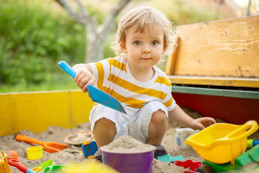 Un niño pequeño jugando en la caja de arena en el patio de recreo al aire libre. Niño pequeño jugando con moldes de arena y haciendo mudpies. Actividades creativas al aire libre para niños photo
