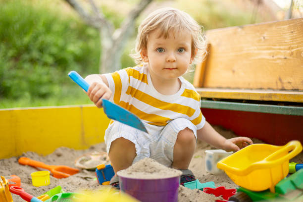 a little boy playing in the sandbox at the playground outdoors. toddler playing with sand molds and making mudpies. outdoor creative activities for kids - alleen babys stockfoto's en -beelden