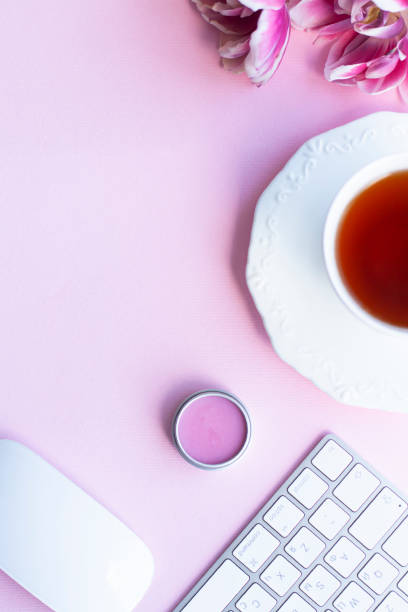 istock Half of black tea cup with pink peony tulips, white wireless keyboard half and mouse, lips balm on pink background 1363654570