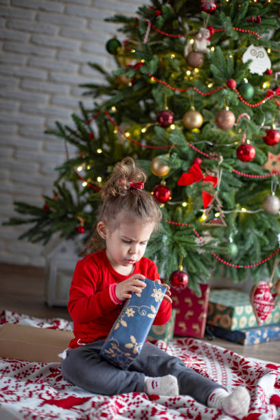istock Cute little toddler opening present near Christmas tree 1363655235