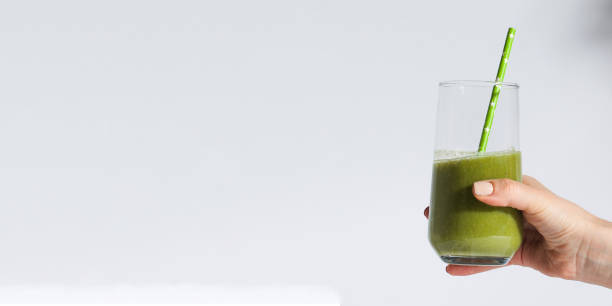 istock A woman's hand holds a glass with green smoothies on a white background. Banner. 1363661319