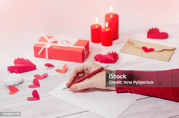 A Womans Hand Writes A Love Letter For Valentines Day An Envelope With A Heart A Gift And Candles Stock Photo - Download Image Now