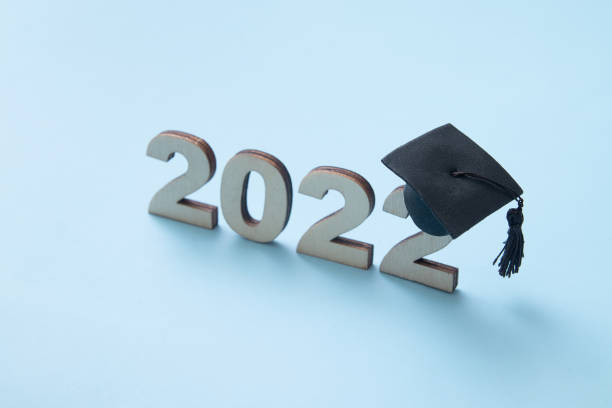 formatura 2022 usando chapéu de pós-graduação no número de madeira 2022 no fundo azul. foco variado - junior high fotos - fotografias e filmes do acervo