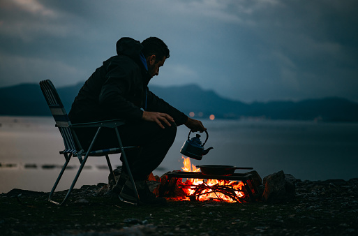 Young Man Making Coffee at Campfire