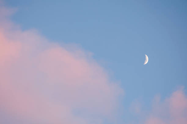 Half white moon on a blue sunset sky with pink clouds