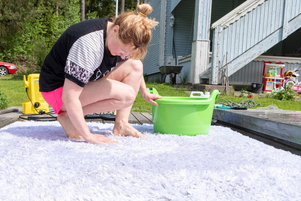 Caucasian woman washes a white carpet, on a wooden terrace, backyard. She uses a powerful solution Caucasian woman washes a white carpet, on a wooden terrace, backyard. She uses a powerful solution vacation rental cleaning stock pictures, royalty-free photos & images