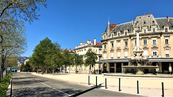 Boulevard of Valence France with old Haussmann style buildings and the monumental fountain on a sunny blue sky.