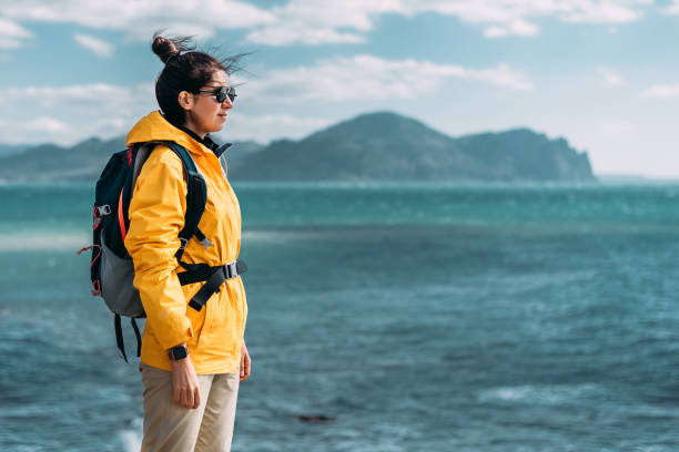 Traveler with his tourist backpack is standing against a sea background. Travel, tourism and active lifestyle concept. Portrait of a female traveler on the background of the blue sea. Copy space stock photo