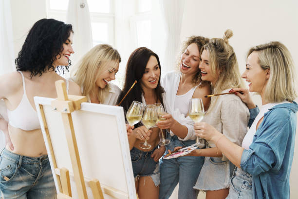 gruppe von frauen malt auf leinwand und trinkt weißwein während der party zu hause - bachelorette party stock-fotos und bilder