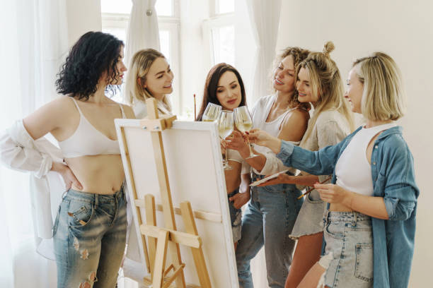 Group of women paint on canvas and drinking white wine during party at home stock photo