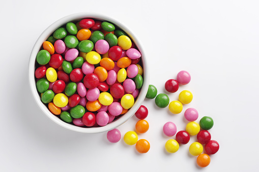 Colorful skittles candies in bowl on white background, top view