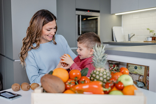 A mother and son holding vegetables and fruits at home