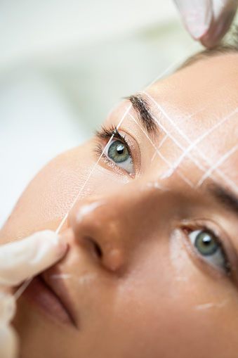 Young woman during professional eyebrow mapping procedure before permanent make-up
