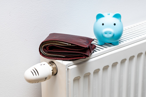 Una billetera de peluche acostada en el radiador y una pequeña alcancía azul, El concepto de aumento de los costos de calefacción del apartamento photo