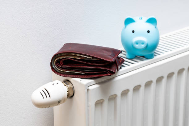 A stuffed wallet lying on the radiator and a small blue piggy bank, The concept of rising apartment heating costs A stuffed wallet lying on the radiator and a small blue piggy bank, The concept of rising apartment heating costs beak stock pictures, royalty-free photos & images