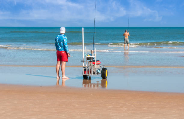 Daytona Beach Fishermen Daytona Beach, Florida, USA-December 29, 2021- Two fishermen wheel their beach cart carrying their fishing supplies and bait to the water's  edge for a day of surf casting on a warm late December afternoon. sea fishing stock pictures, royalty-free photos & images