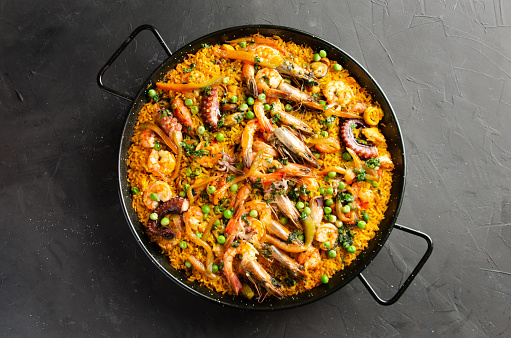 Paella served in paella pan on black background. Flat view