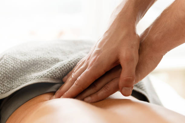 крупный план мужских рук массажиста во время массажа спины для молодой женщины - masseur стоковые фото и изображения