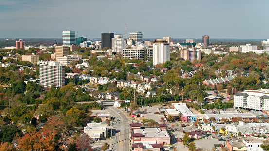 Aerial shot of Columbia, South Carolina from over the Five Points neighborhood, looking across the rooftops and the University of South Carolina campus towards downtown office towers and the state house.