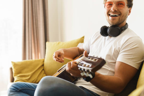 istock Young man on sofa is playing acoustic guitar 1363689381