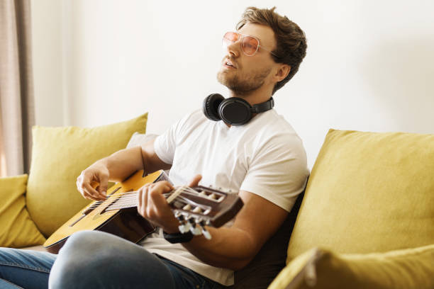 istock Young man on sofa is playing acoustic guitar 1363689408