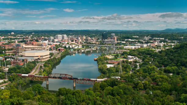 Aerial View of Knoxville Surrounded by Forest Aerial shot of Knoxville, Tennessee on a sunny and beautiful day in early Fall, looking down on the city from over the hills, along the Tennessee River past the University of Tennessee towards the downtown. A freight train is stopped on a bridge.     

Authorization was obtained from the FAA for this operation in restricted airspace. tennessee stock pictures, royalty-free photos & images