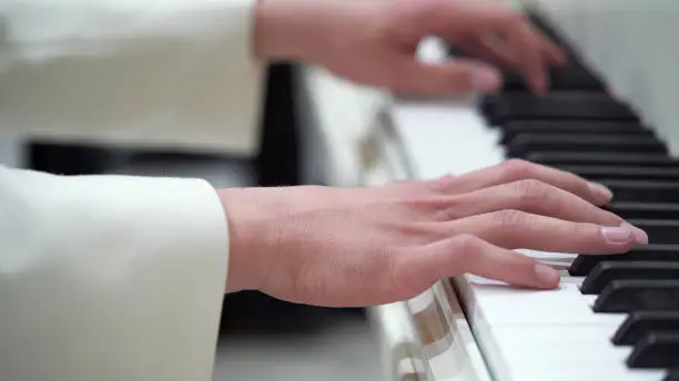 Close-up hands of a young man in a white jacket play music on the piano.Classical music, concert, performance.Music lessons on the piano, keyboard instrument.Macro photography.Selective focus