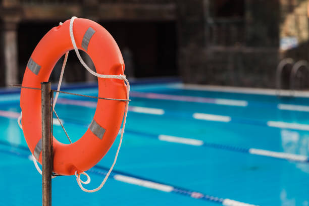 Lifeguard standing poolside holding a lifebuoy, ensuring safety at a luxurious hotel pool on a bright sunny day