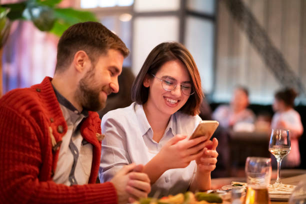 istock Smiling young couple using a smartphone together at the restaurant 1363698654