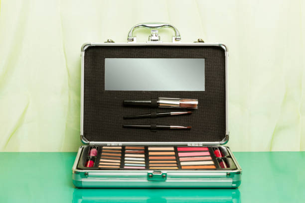 A silver aluminum open makeup case with eye shadows, blushes, pencils and brushes on a green background.